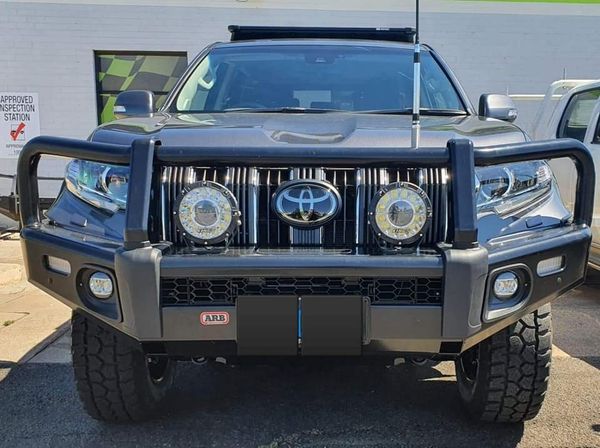 A Toyota Prado fitted with an ARB bull bar and a pair of driving lights, parked in front of the Approved Inspection Station sign